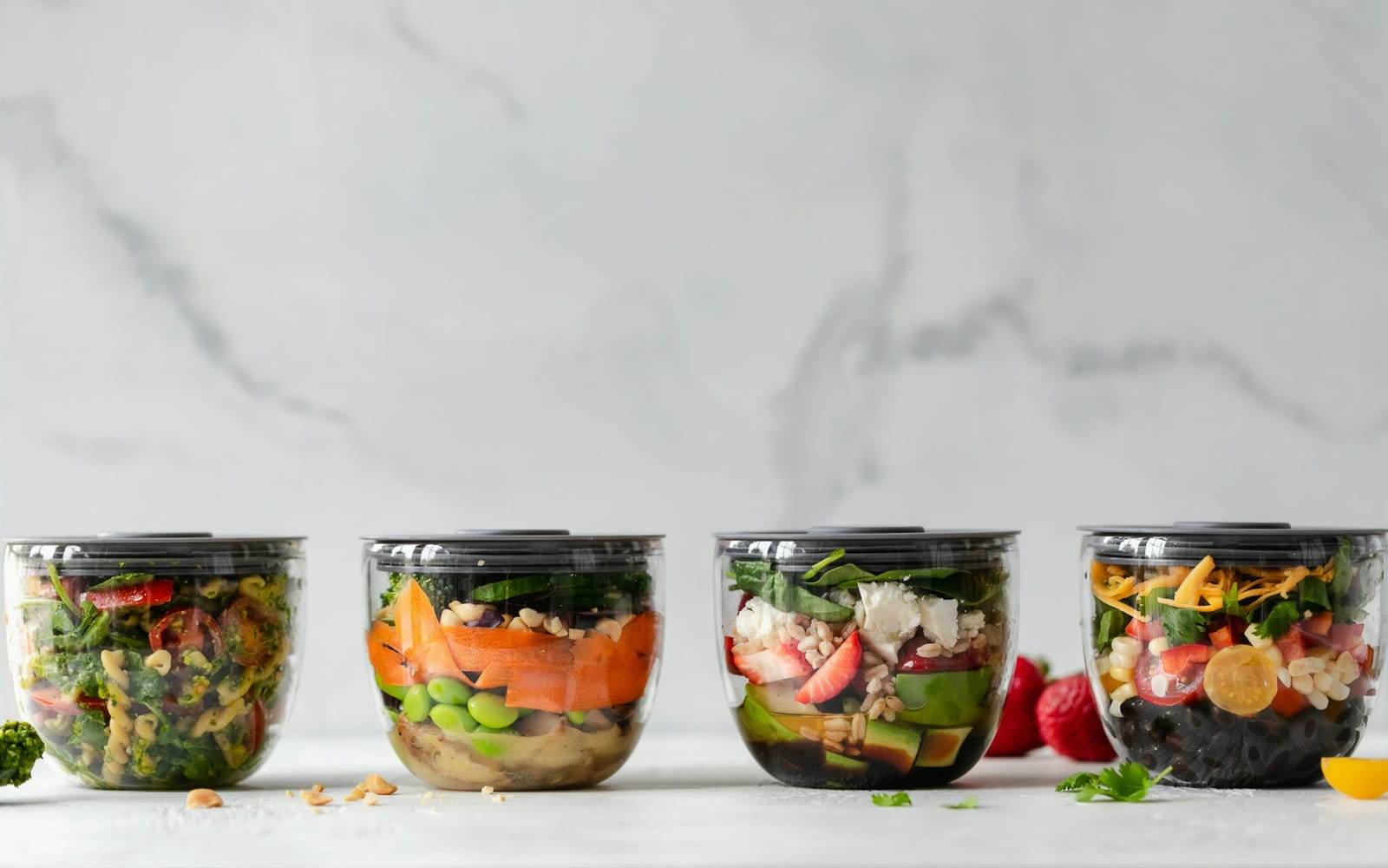 Four clear meal-prep bowls of salad lined up on a marble counter